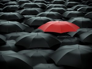 Red umbrella over many black umbrellas